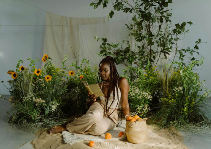 a photo of a black woman sitting in a fake garden photoshoot background reading a book.