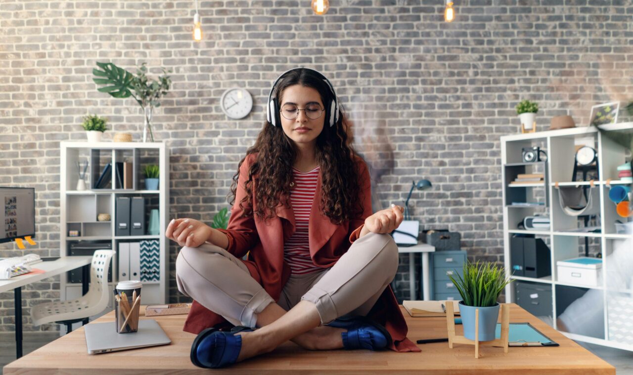 a woman sitting on top of a table meditating with her eyes clothes wearing headphones.