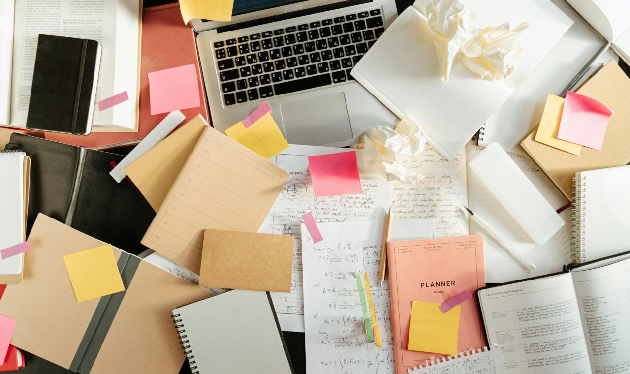 a messy desk with a laptop, notebooks, and trash.