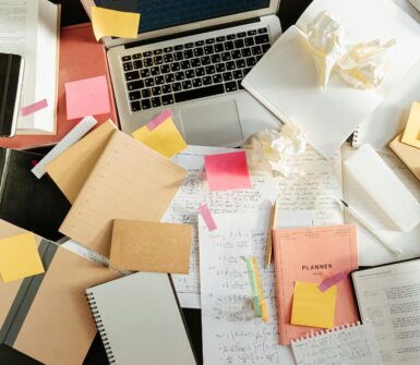 a messy desk with a laptop, notebooks, and trash.