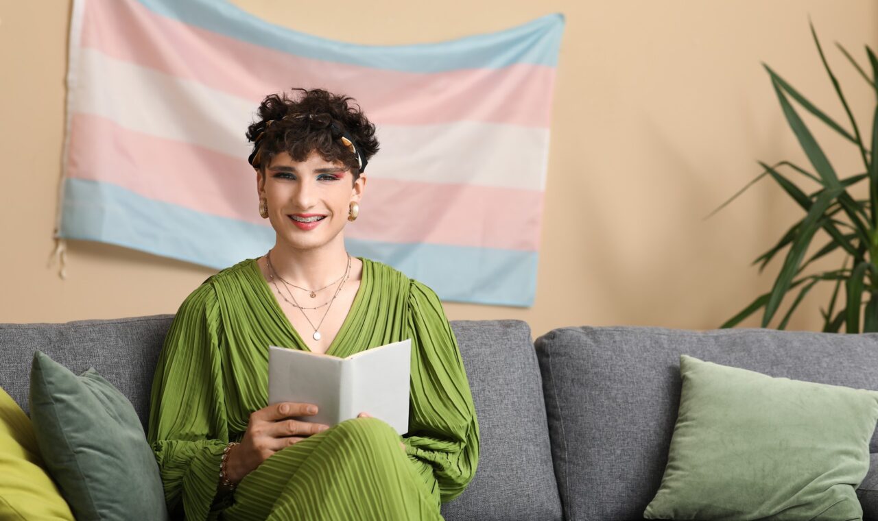 Young transgender woman reading book on sofa at home