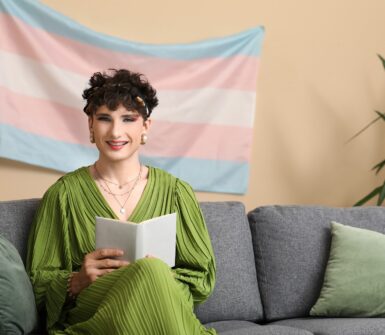 Young transgender woman reading book on sofa at home