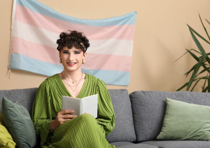 Young transgender woman reading book on sofa at home
