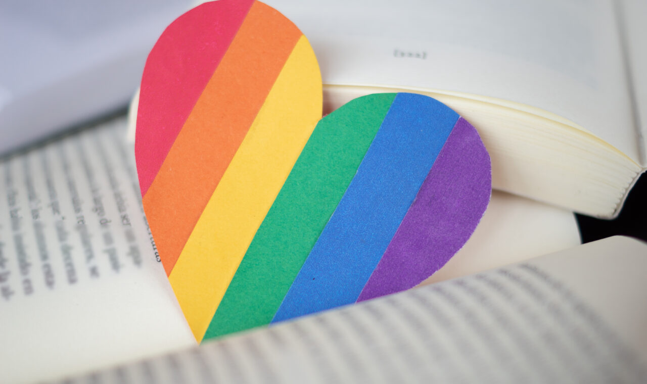 an image of pride flag shaped as a heart lying between the two pages of a book.