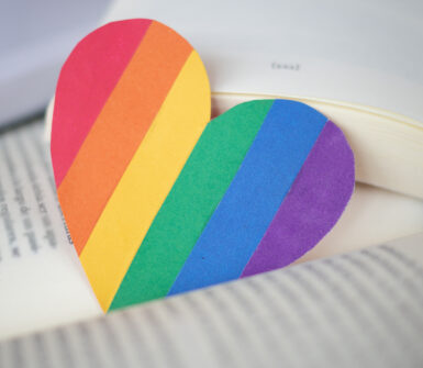 an image of pride flag shaped as a heart lying between the two pages of a book.