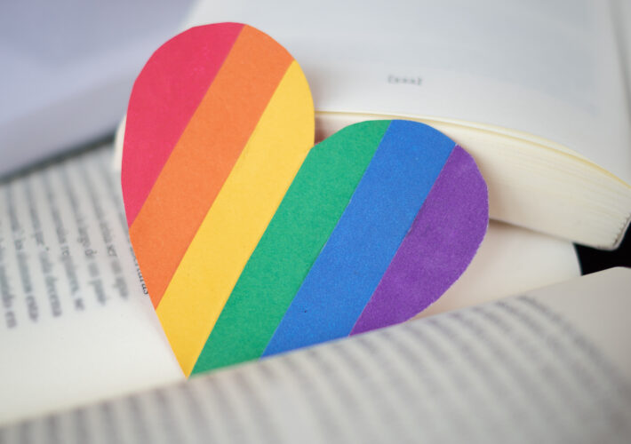an image of pride flag shaped as a heart lying between the two pages of a book.