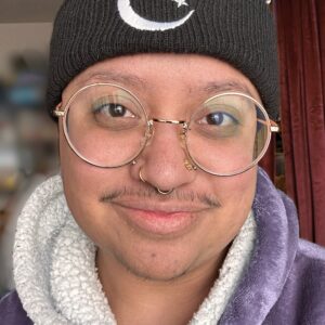 headshot of author Felix Graves. A handsome Indonesian trans man wearing a bini hat and large round glasses. 