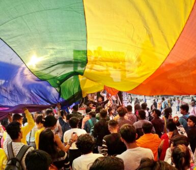 Joyful crowd celebrating Pride Parade under rainbow flag in Kolkata, India.