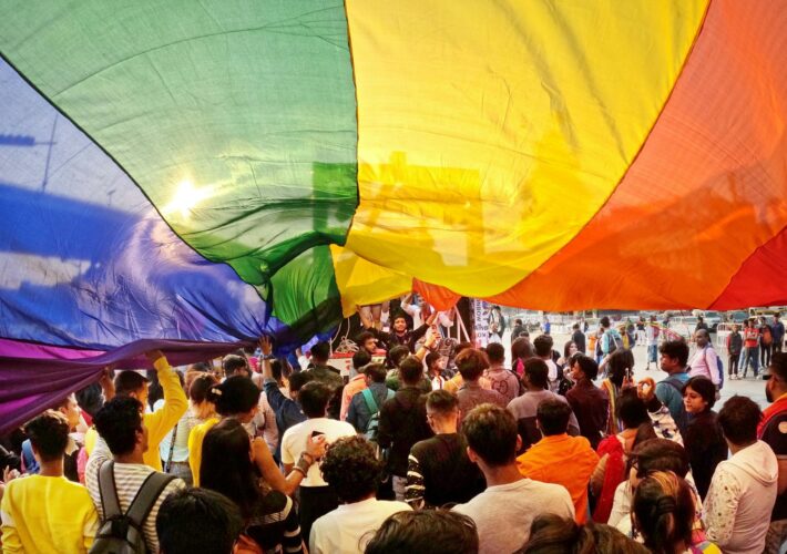 Joyful crowd celebrating Pride Parade under rainbow flag in Kolkata, India.