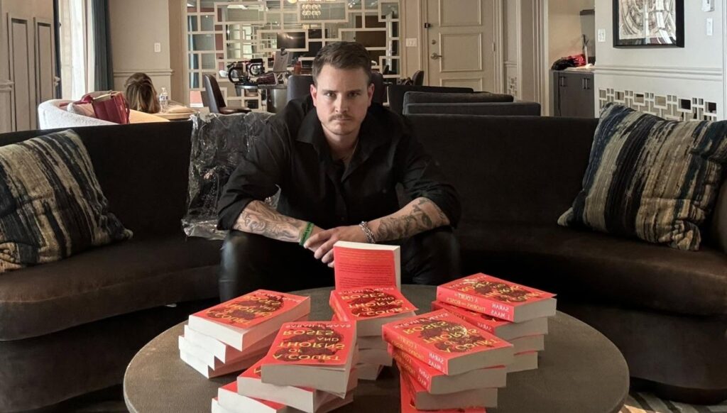 a photo of booktoker PB Squamer sitting in a sofa in front of a large stack of Sarah J. Maas books. 