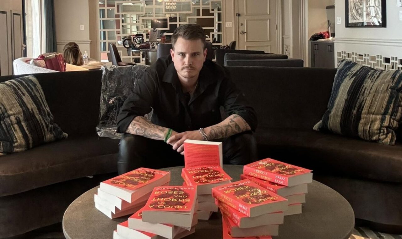 a photo of booktoker PB Squamer sitting in a sofa in front of a large stack of Sarah J. Maas books.