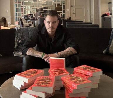 a photo of booktoker PB Squamer sitting in a sofa in front of a large stack of Sarah J. Maas books.