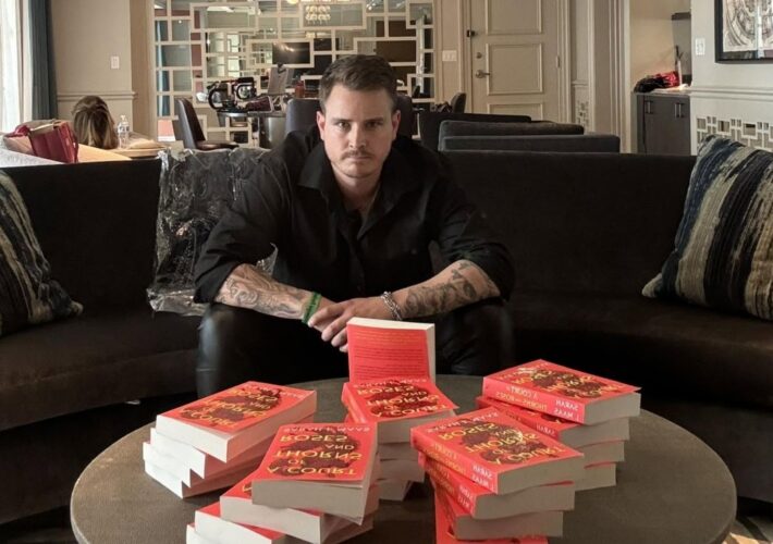 a photo of booktoker PB Squamer sitting in a sofa in front of a large stack of Sarah J. Maas books.