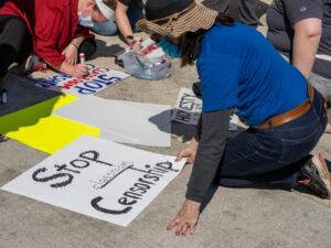 Protesters create signs reading “Stop Censorship” during an outdoor rally,