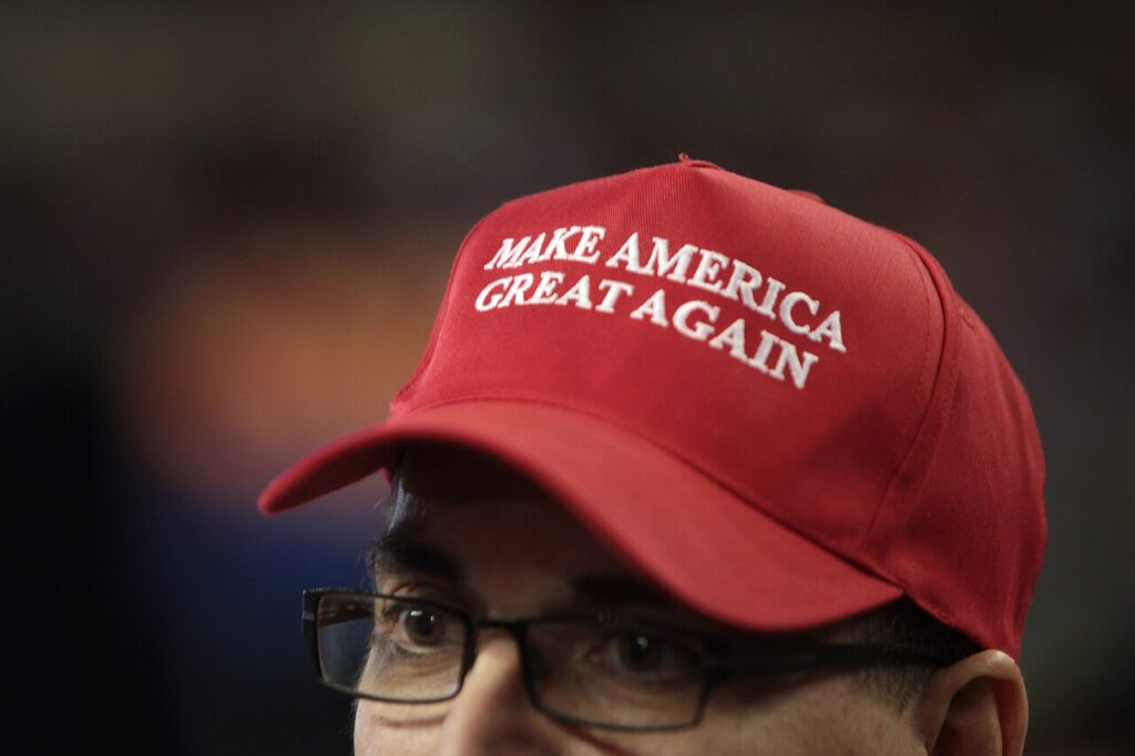 Close-up of a person wearing glasses and a red cap reading “MAKE AMERICA GREAT AGAIN."
