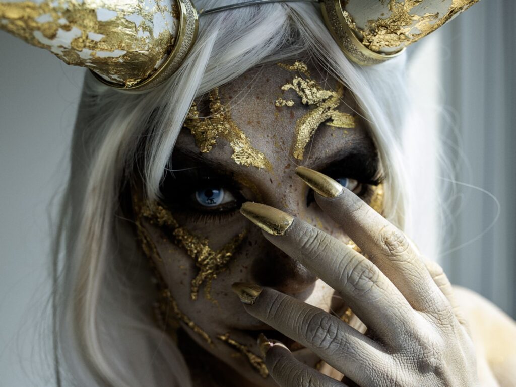 an image of a female demon with long white hair, golden skin, and and golden claws. 